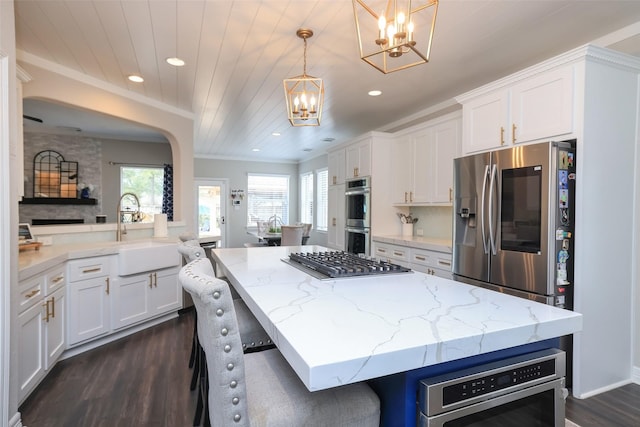 kitchen with sink, hanging light fixtures, stainless steel appliances, a kitchen breakfast bar, and white cabinets