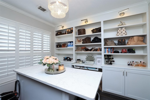 interior space featuring white cabinetry, crown molding, a center island, and light stone countertops