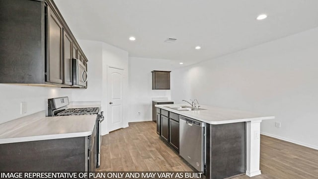 kitchen featuring appliances with stainless steel finishes, an island with sink, sink, dark brown cabinetry, and light wood-type flooring