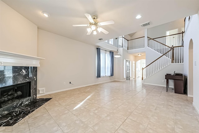 unfurnished living room featuring ceiling fan, a towering ceiling, light tile patterned flooring, and a high end fireplace