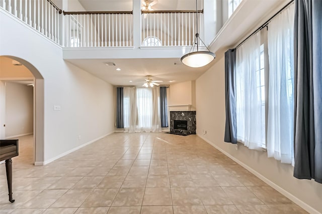 unfurnished living room featuring a high ceiling, a premium fireplace, light tile patterned floors, and ceiling fan