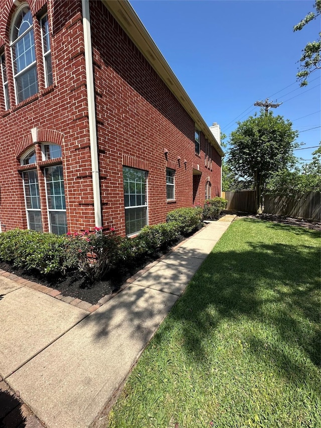 view of home's exterior with brick siding, a chimney, fence, and a lawn