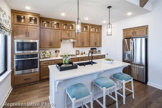 kitchen featuring a breakfast bar, a sink, stainless steel appliances, brown cabinets, and dark wood-style floors