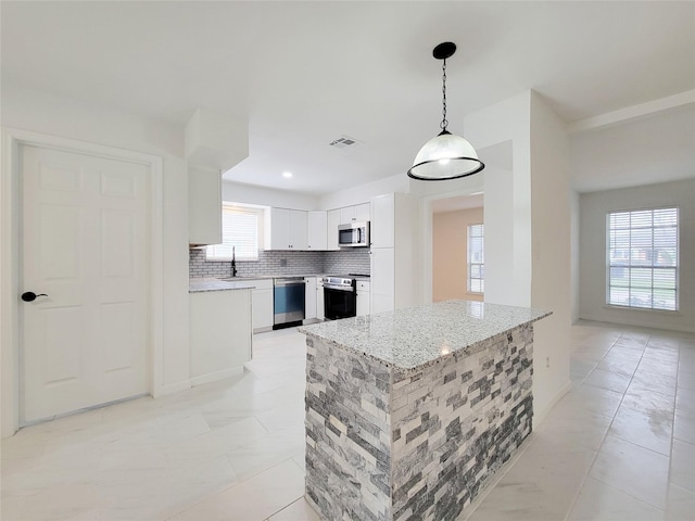 kitchen featuring hanging light fixtures, white cabinets, stainless steel appliances, light stone countertops, and backsplash