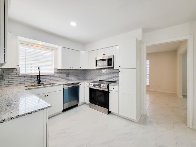 kitchen featuring white cabinetry, sink, light stone countertops, and appliances with stainless steel finishes