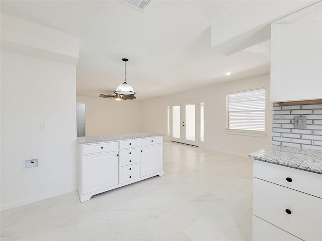 kitchen with tasteful backsplash, white cabinetry, pendant lighting, and light stone counters