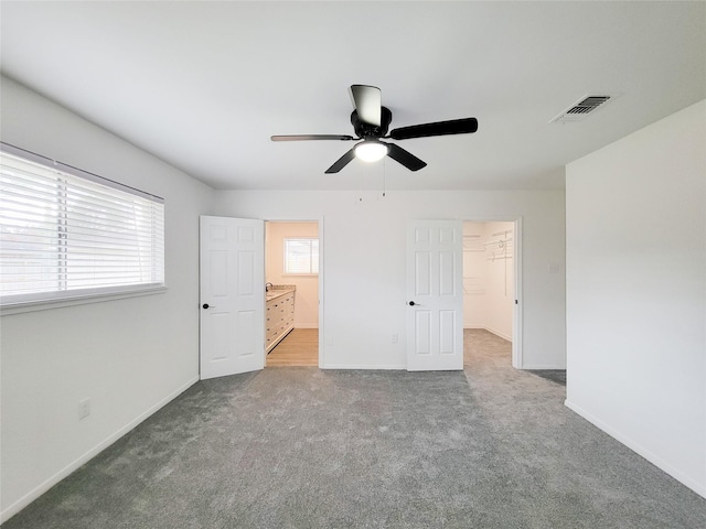 unfurnished bedroom featuring multiple windows, a walk in closet, ceiling fan, and carpet flooring