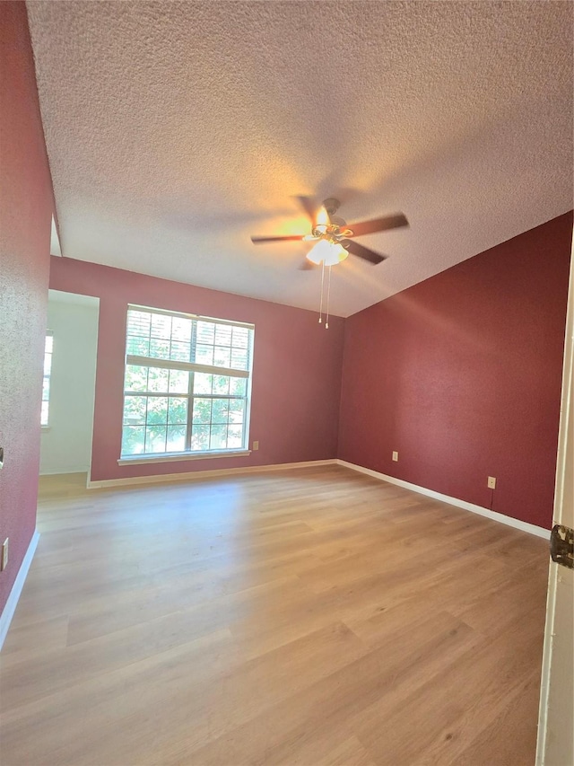 empty room with a textured ceiling, light hardwood / wood-style flooring, ceiling fan, and plenty of natural light