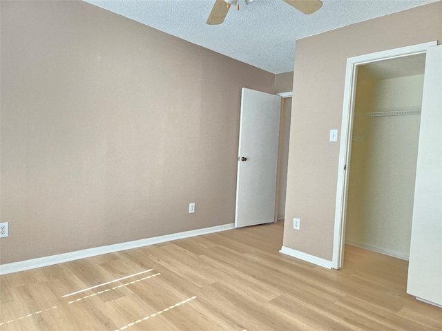 unfurnished bedroom with a walk in closet, ceiling fan, light hardwood / wood-style floors, a textured ceiling, and a closet