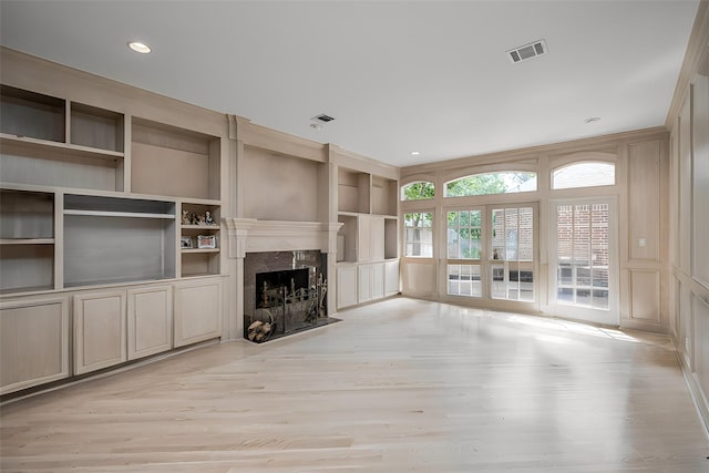 unfurnished living room with visible vents, a premium fireplace, built in features, and a decorative wall