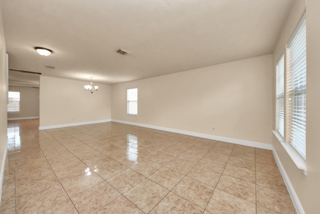 tiled spare room featuring a notable chandelier