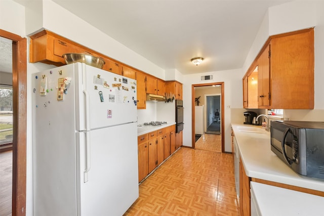 kitchen with stainless steel gas cooktop, sink, white fridge, light parquet flooring, and oven