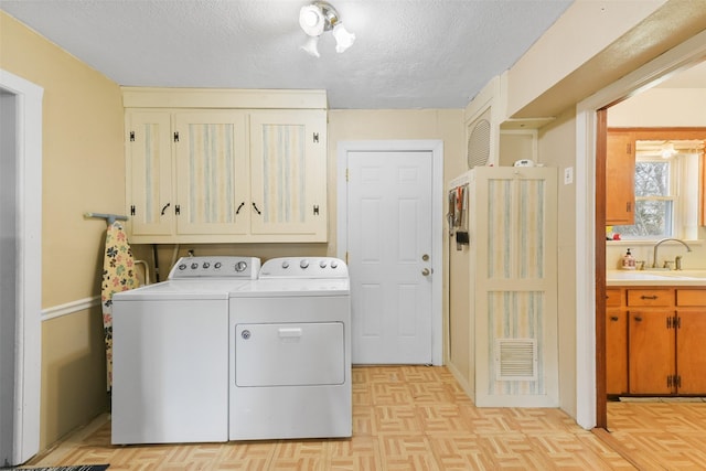 clothes washing area featuring sink, cabinets, a textured ceiling, light parquet flooring, and washer and clothes dryer