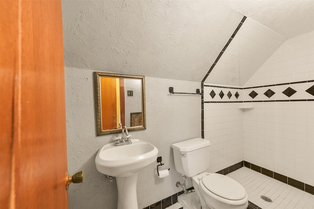 bathroom featuring toilet, vaulted ceiling, a textured ceiling, and a tile shower