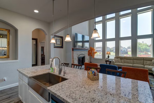 kitchen with a stone fireplace, sink, hanging light fixtures, dark hardwood / wood-style floors, and light stone countertops