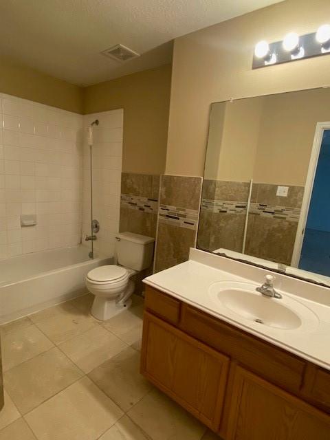 full bathroom with tile walls, vanity, tile patterned floors, toilet, and tiled shower / bath