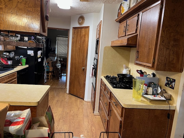 kitchen featuring sink, a textured ceiling, light wood-type flooring, and black appliances