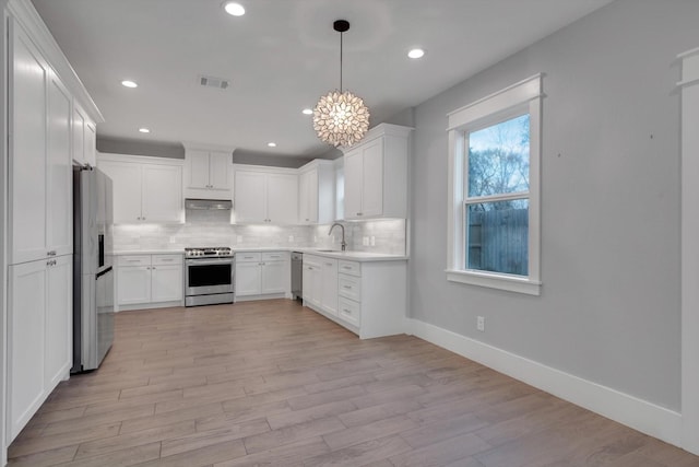 kitchen with white cabinetry, stainless steel appliances, tasteful backsplash, decorative light fixtures, and light wood-type flooring