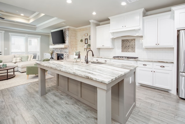 kitchen featuring sink, a center island with sink, white cabinets, and light stone counters