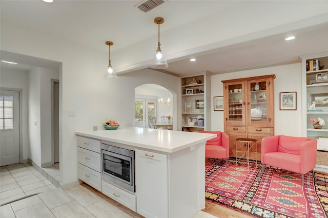 kitchen with pendant lighting, light tile patterned floors, built in features, white cabinetry, and stainless steel microwave