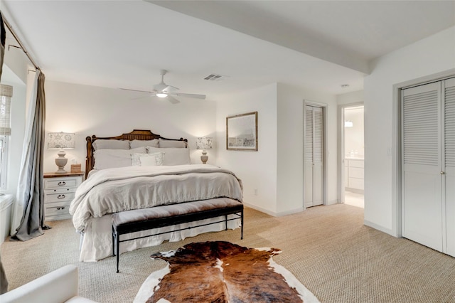 bedroom with multiple closets, ensuite bathroom, light carpet, and ceiling fan