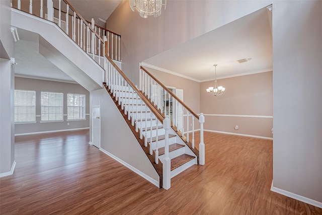 staircase with hardwood / wood-style flooring, a towering ceiling, ornamental molding, and a notable chandelier