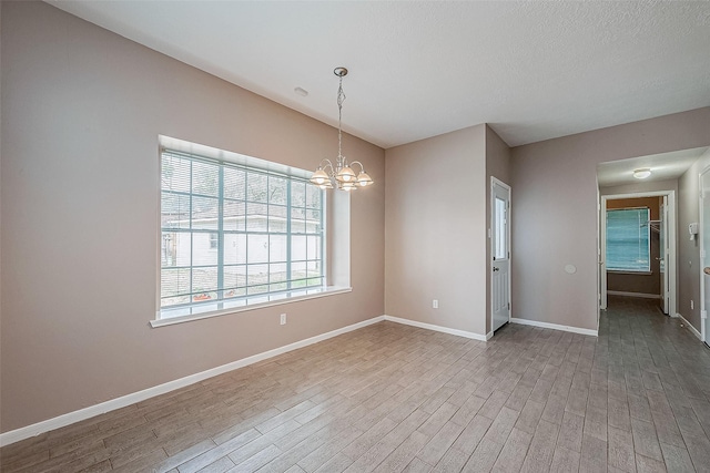 spare room featuring a textured ceiling, a chandelier, and light hardwood / wood-style flooring