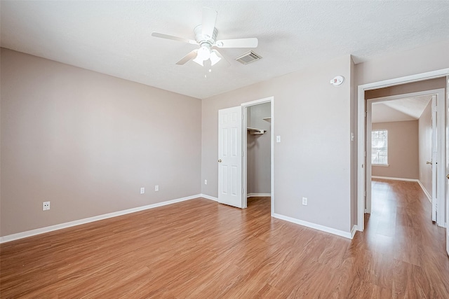 unfurnished bedroom featuring ceiling fan, a spacious closet, a textured ceiling, and light wood-type flooring