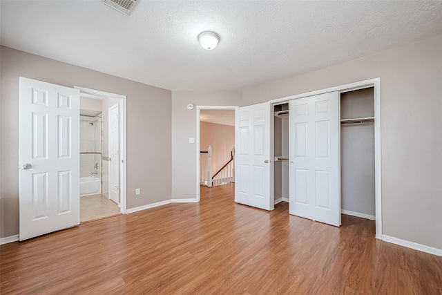 unfurnished bedroom with connected bathroom, a closet, a textured ceiling, and light wood-type flooring