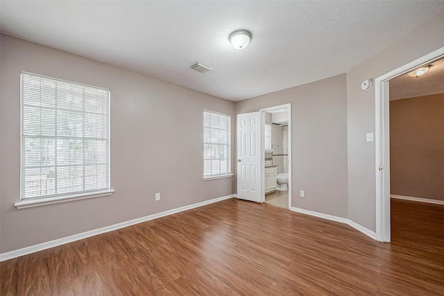 unfurnished bedroom featuring connected bathroom, hardwood / wood-style floors, and a textured ceiling