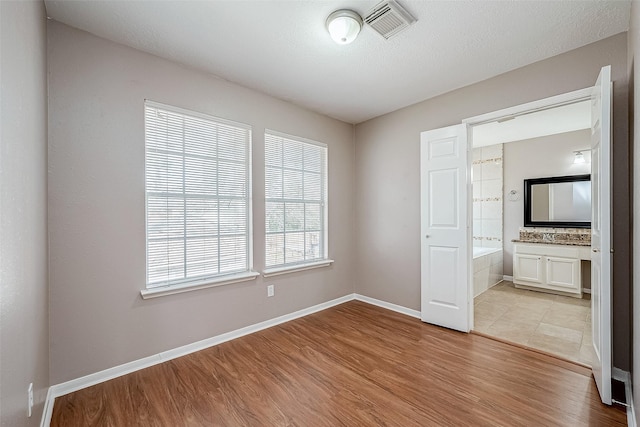 unfurnished bedroom with a textured ceiling, ensuite bath, and light hardwood / wood-style flooring