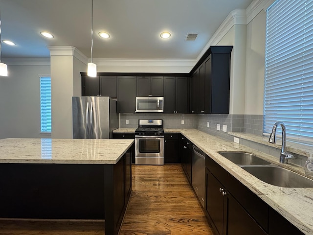 kitchen with light stone counters, stainless steel appliances, sink, and hanging light fixtures