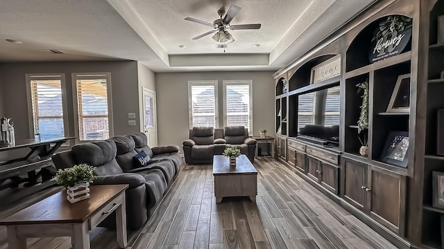 living room with ceiling fan, a tray ceiling, and a textured ceiling