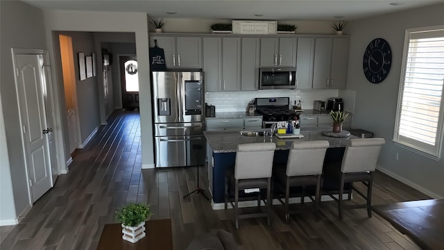 kitchen with dark hardwood / wood-style floors, an island with sink, a kitchen breakfast bar, stainless steel appliances, and light stone countertops