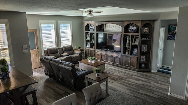 living room featuring ceiling fan, dark wood-type flooring, and a textured ceiling