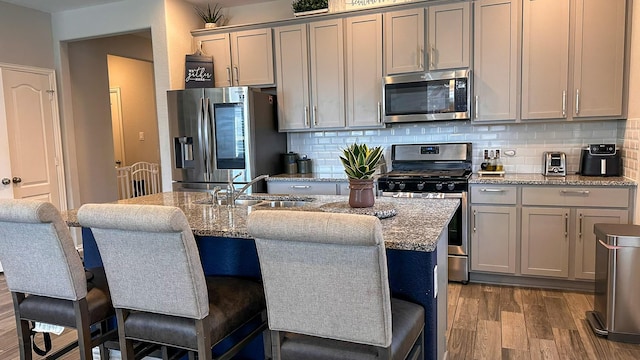 kitchen featuring gray cabinets, a breakfast bar, stainless steel appliances, light stone counters, and a center island with sink