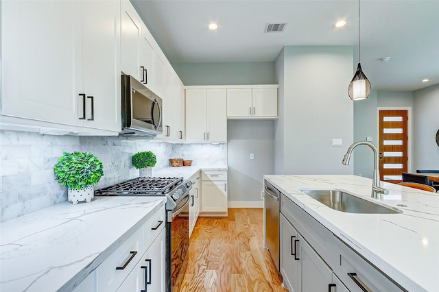 kitchen with sink, appliances with stainless steel finishes, light stone countertops, white cabinets, and decorative light fixtures