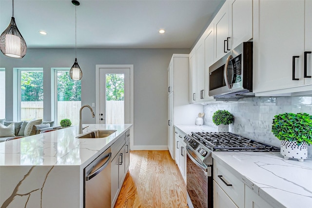 kitchen with appliances with stainless steel finishes, white cabinetry, sink, light stone counters, and a center island with sink