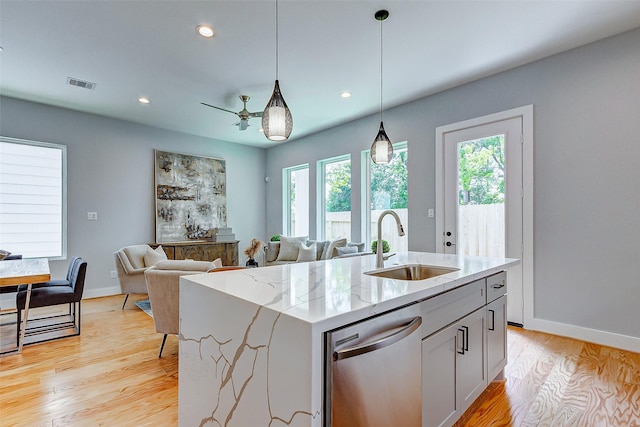 kitchen with sink, light stone counters, stainless steel dishwasher, pendant lighting, and a kitchen island with sink