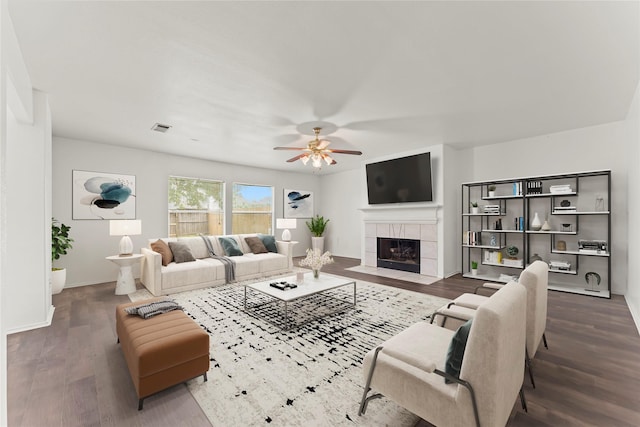 living room featuring a tiled fireplace, dark wood-type flooring, and ceiling fan