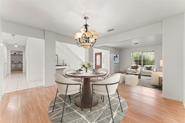 dining space featuring washing machine and clothes dryer, a notable chandelier, and light hardwood / wood-style flooring