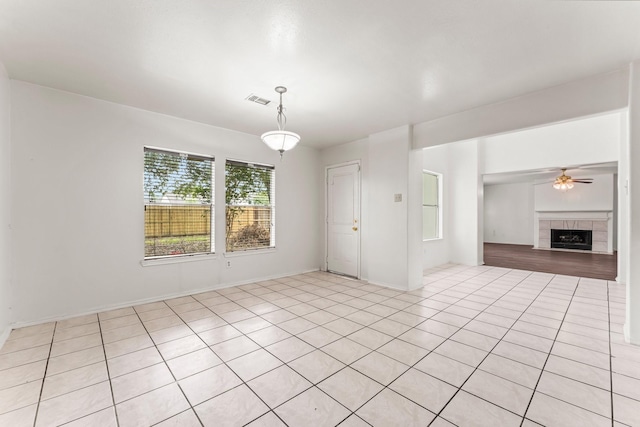 unfurnished living room featuring a tile fireplace, light tile patterned floors, and ceiling fan