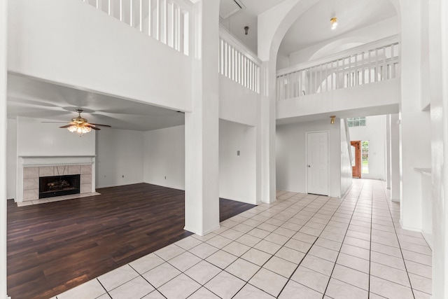 unfurnished living room featuring a tiled fireplace, light tile patterned flooring, a high ceiling, and ceiling fan