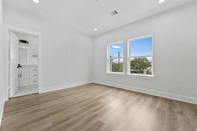 unfurnished bedroom with ensuite bathroom and light wood-type flooring