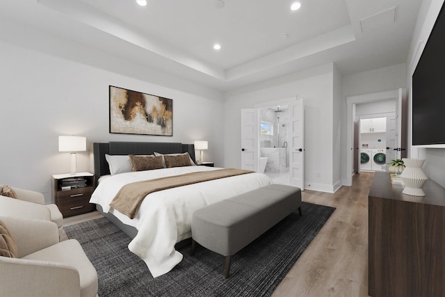 bedroom with connected bathroom, a tray ceiling, light hardwood / wood-style floors, and washing machine and clothes dryer