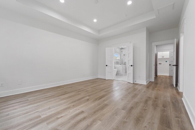 empty room featuring a tray ceiling and light hardwood / wood-style floors