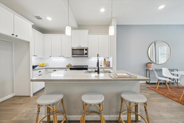 kitchen with pendant lighting, white cabinets, stove, a kitchen island with sink, and light wood-type flooring