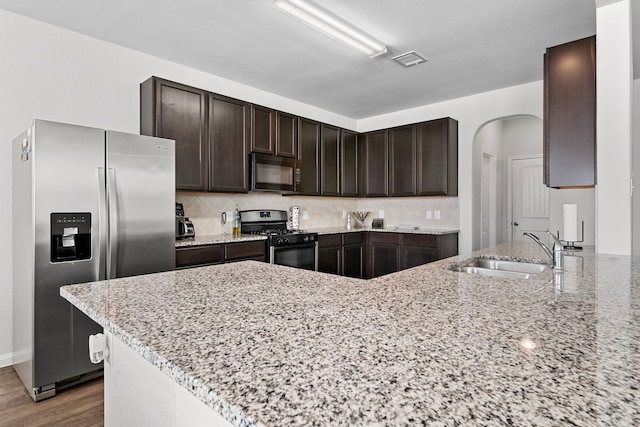 kitchen with sink, stainless steel fridge, backsplash, light stone countertops, and range with gas cooktop