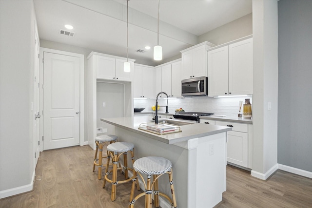 kitchen with light wood-type flooring, appliances with stainless steel finishes, a kitchen island with sink, decorative backsplash, and white cabinets