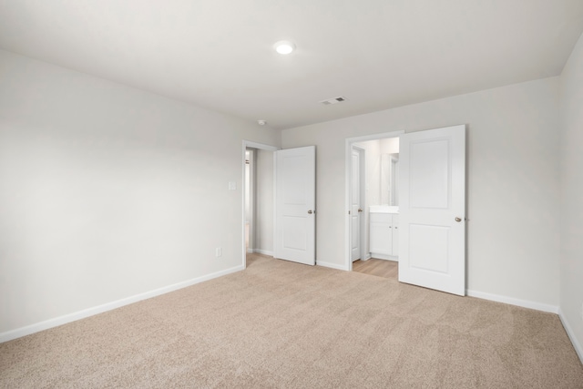 unfurnished bedroom with ensuite bath and light carpet